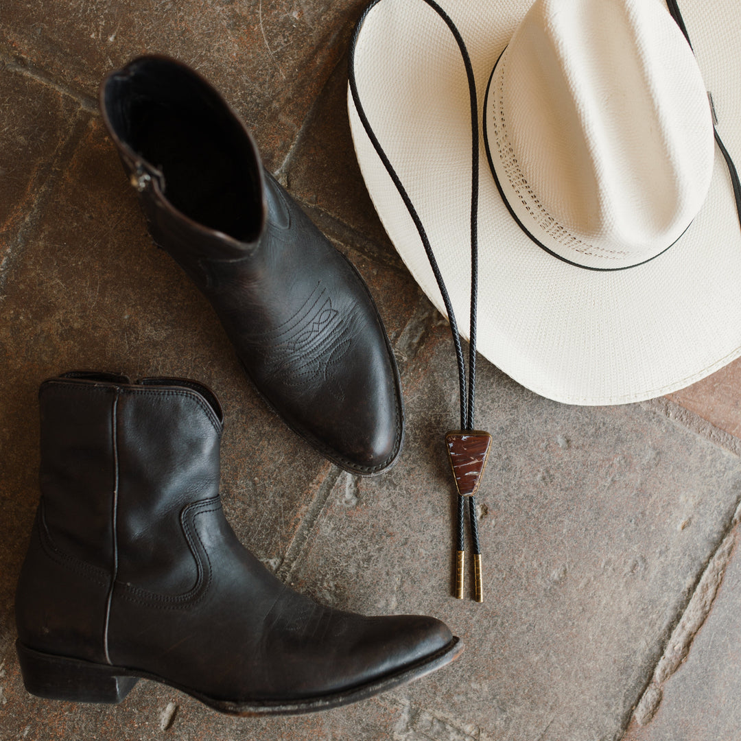 Black boots, Rattlesnake Jasper Bolo Tie, white cowboy hat on a stone floor