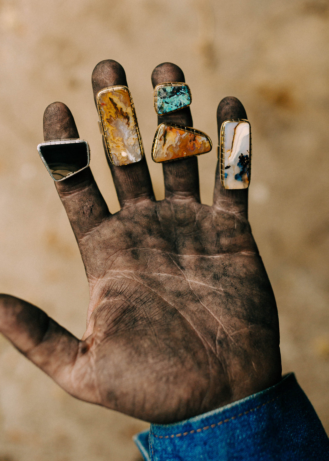 Hand with multiple rings featuring colorful gemstones against a blurred background