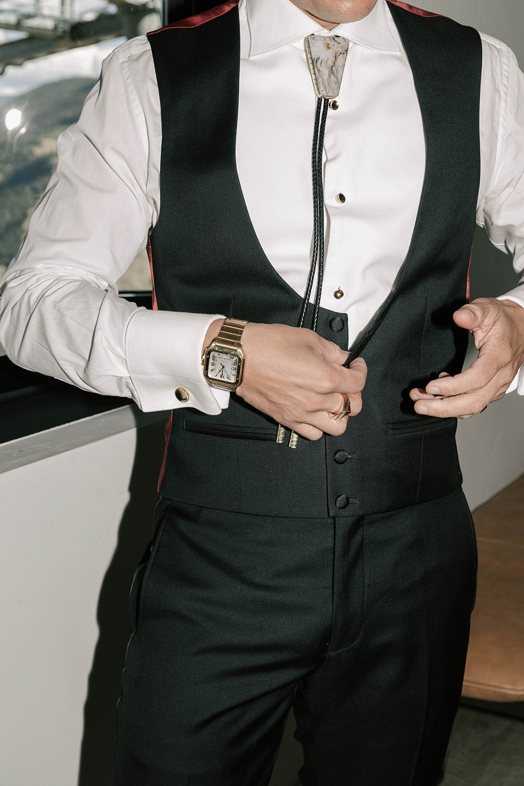 Groom wearing a black vest with a white shirt and a bolo tie.