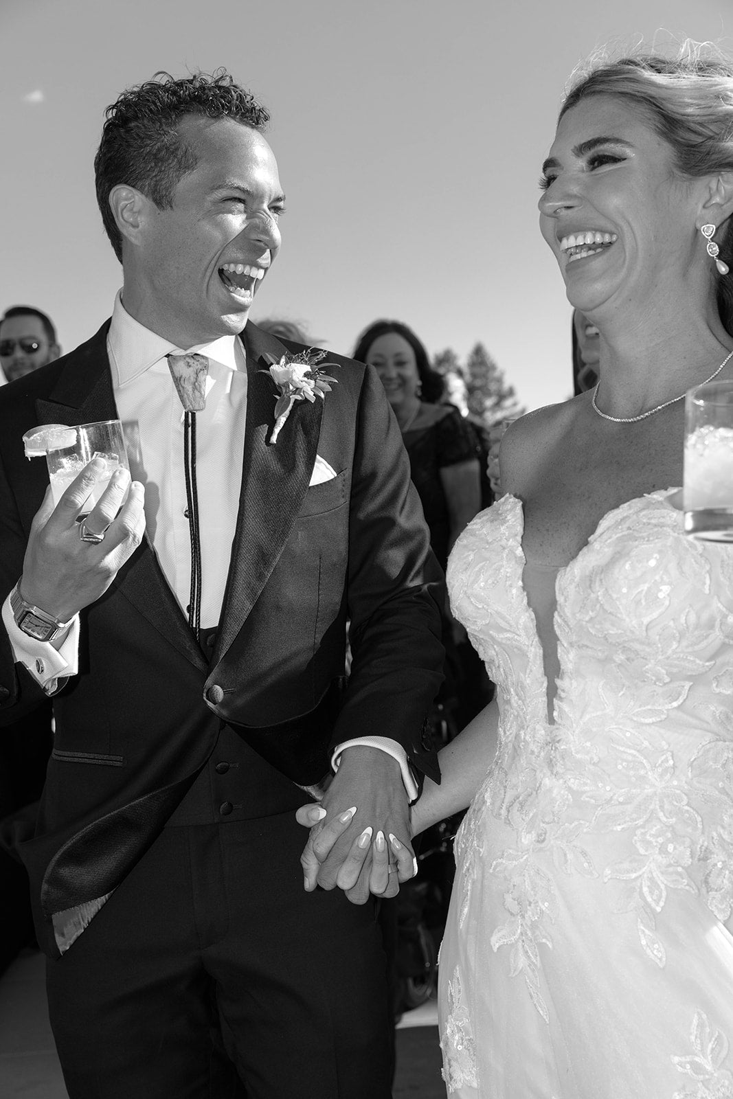 Black and white photo of groom wearing a bolo tie and bride holding cocktails 