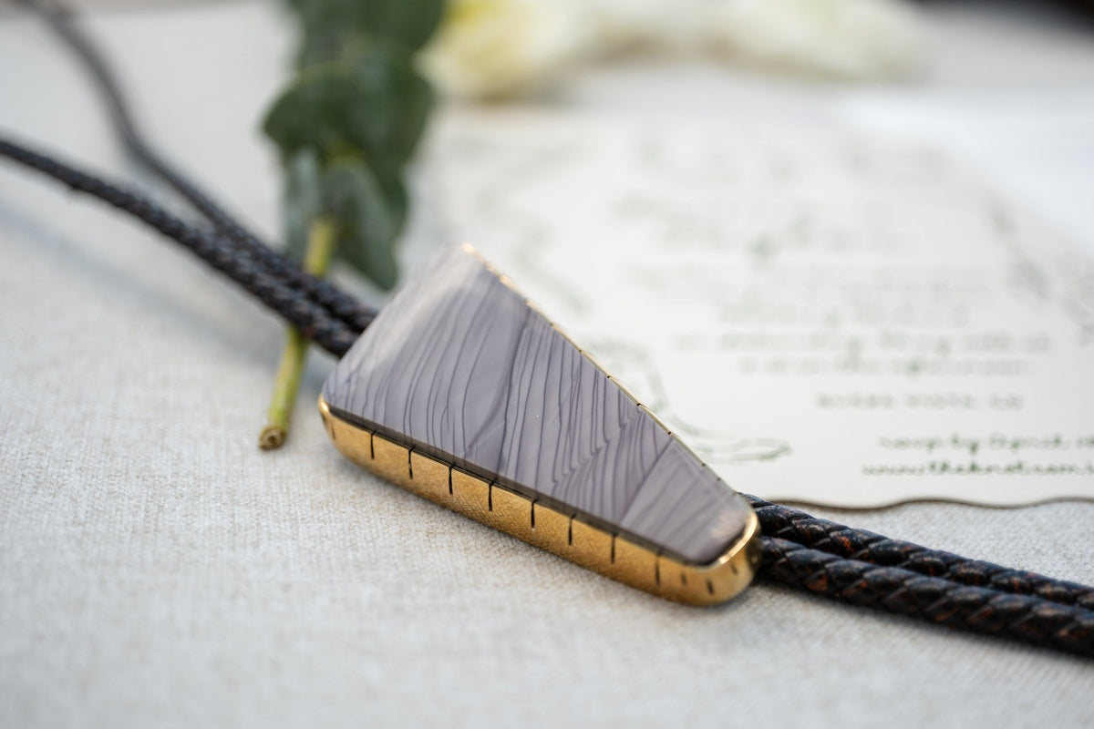 Close-up of a handcrafted wedding bolo tie with a polished gemstone and gold bezel on braided leather cord